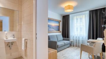 A modern hotel room with a shower, sink, and a seating area with a sofa and chairs.