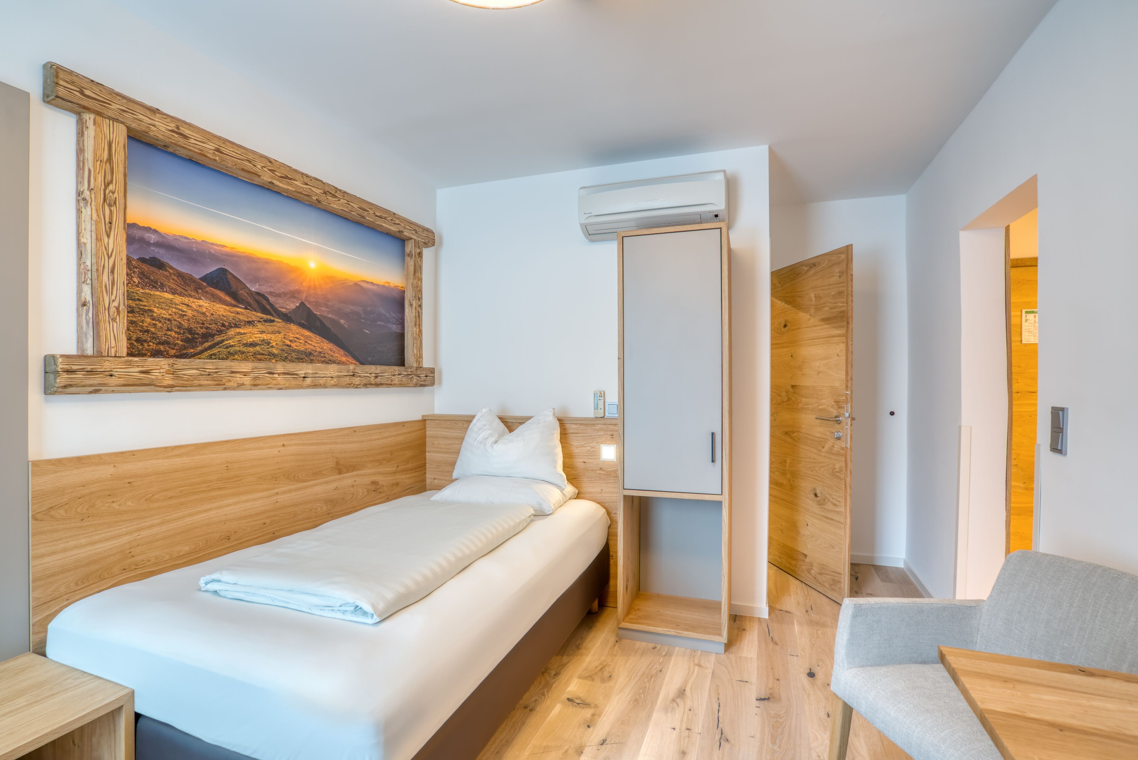 A hotel room with a wooden bed, a painting of a sunset, a wardrobe, and a seating area.