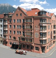 A multi-story hotel with a red facade, balconies with flower boxes, and a sign indicating a restaurant.