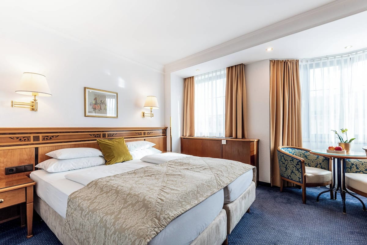 A hotel room with a large bed, two bedside tables, a desk with a chair, and a window with curtains.