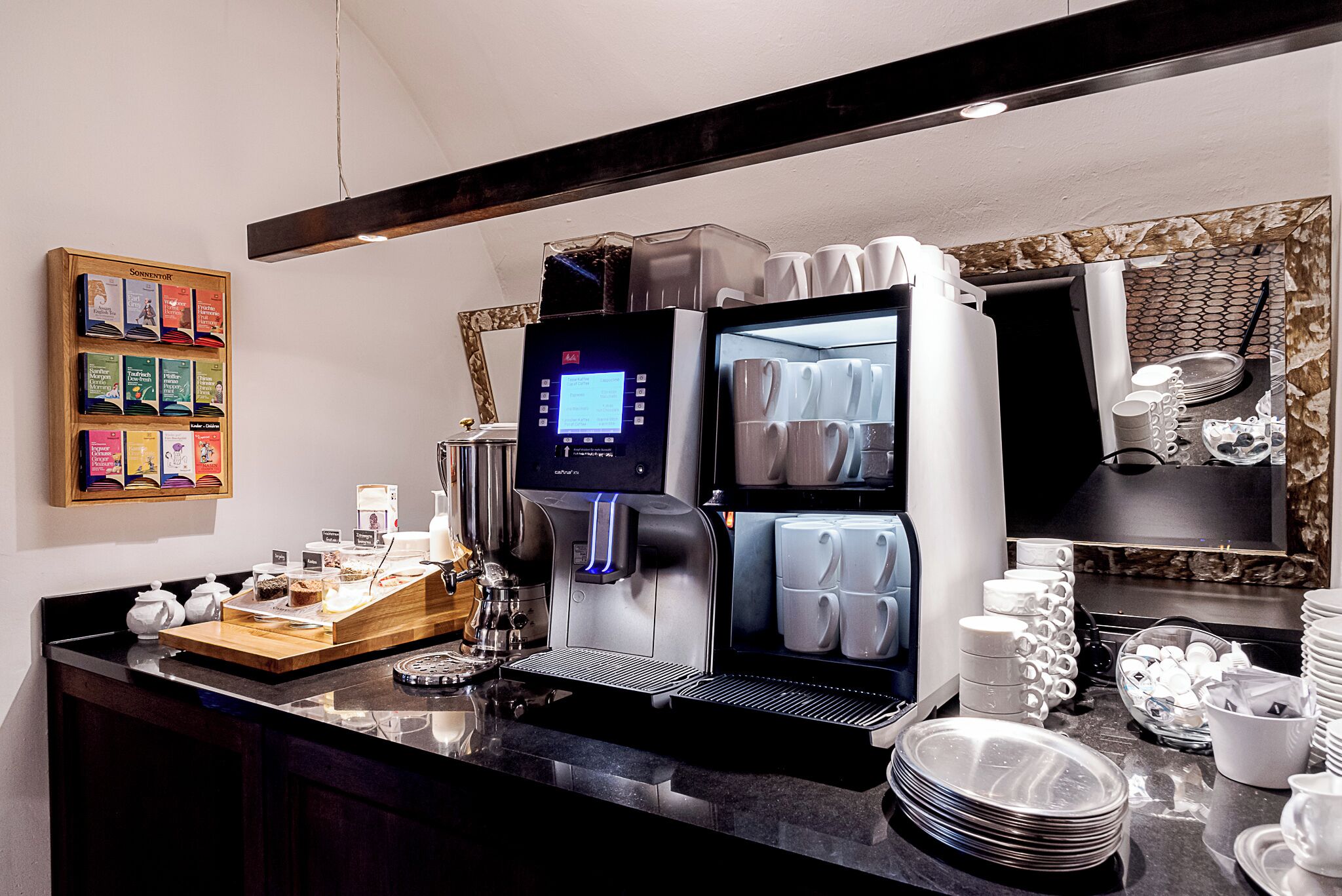 Een koffiehoek met een moderne espressomachine, een presentatie van koffieboekjes, en netjes gestapelde bekers en borden.