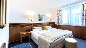 Une chambre d’hôtel avec un grand lit, des tables de chevet, un petit tabouret et une fenêtre avec des rideaux.