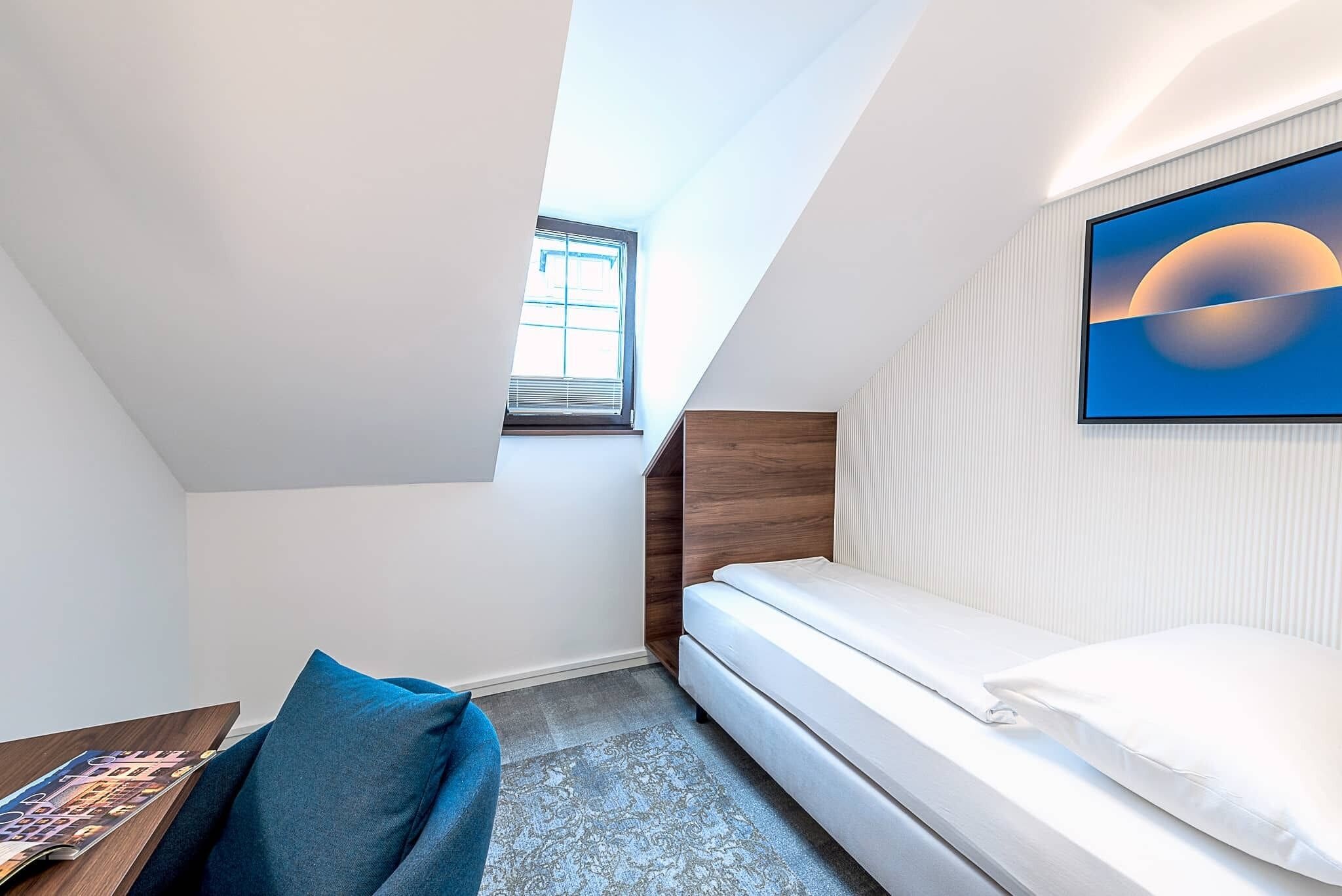 A modern bedroom with a skylight, a bed, a desk, and a wall-mounted TV.