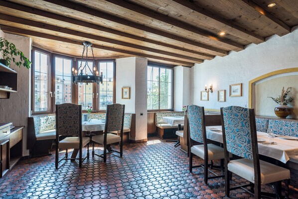 A restaurant interior with wooden beams, patterned floor tiles, and seating with patterned upholstery. - Hotel Mondschein (Innsbruck)