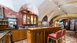 A bar area with a wooden counter, bar stools, and a tiled floor. - Hotel Mondschein (Innsbruck)