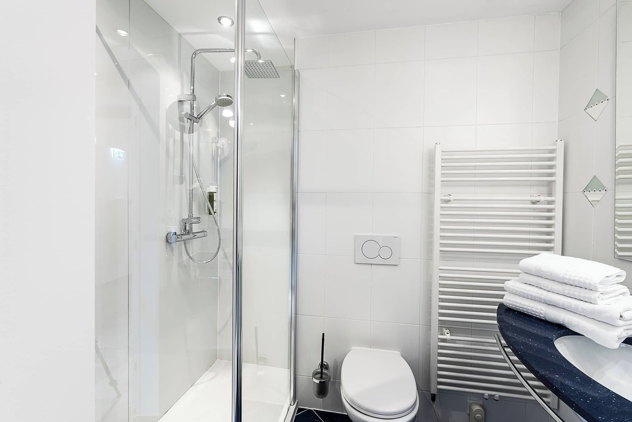 Un baño moderno con ducha de vidrio, inodoro blanco y toallero empotrado.