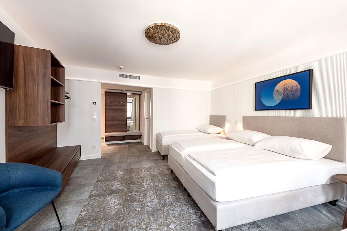 A hotel room with a large bed, a desk, a chair, and a wall-mounted TV.