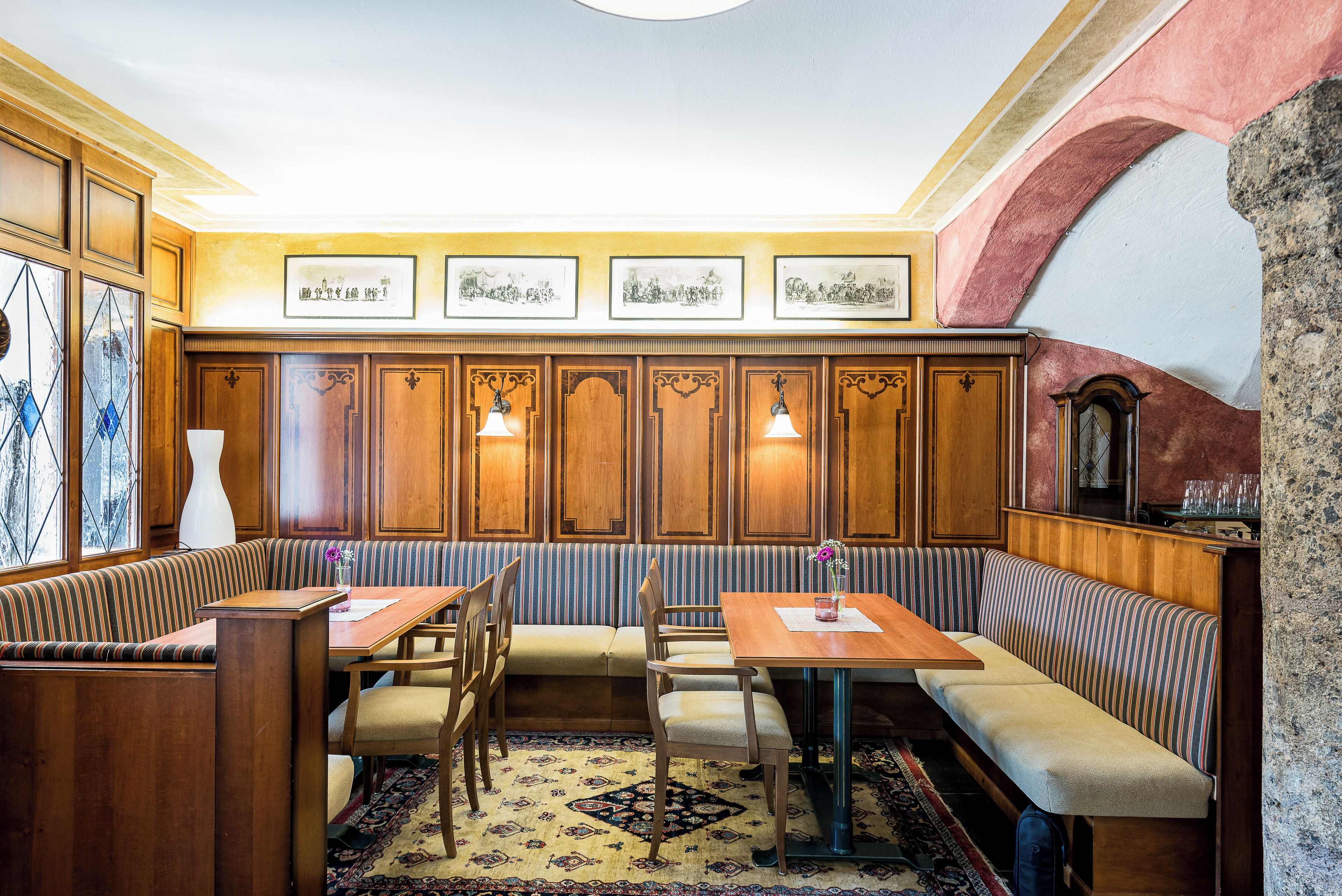 Uma sala de jantar tradicional com painéis de madeira, disposição de assentos em bancos e um tapete estampado.