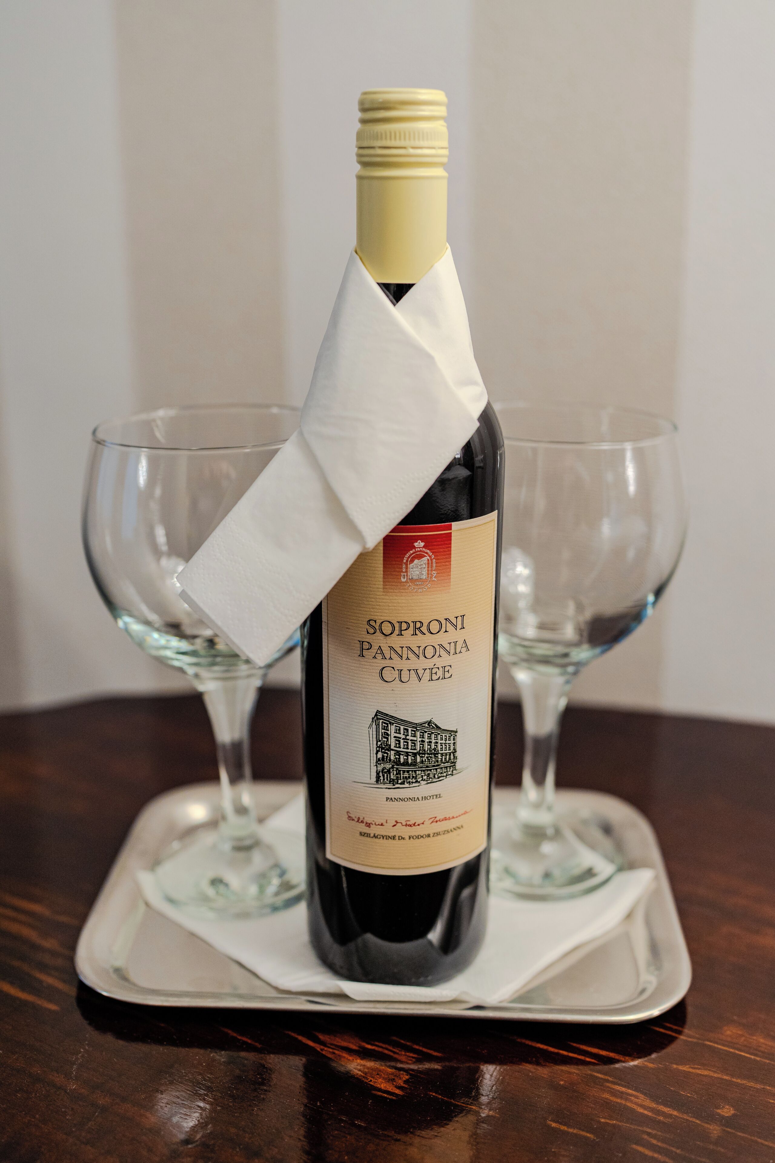 A bottle of wine with a label, placed on a tray with two empty glasses.