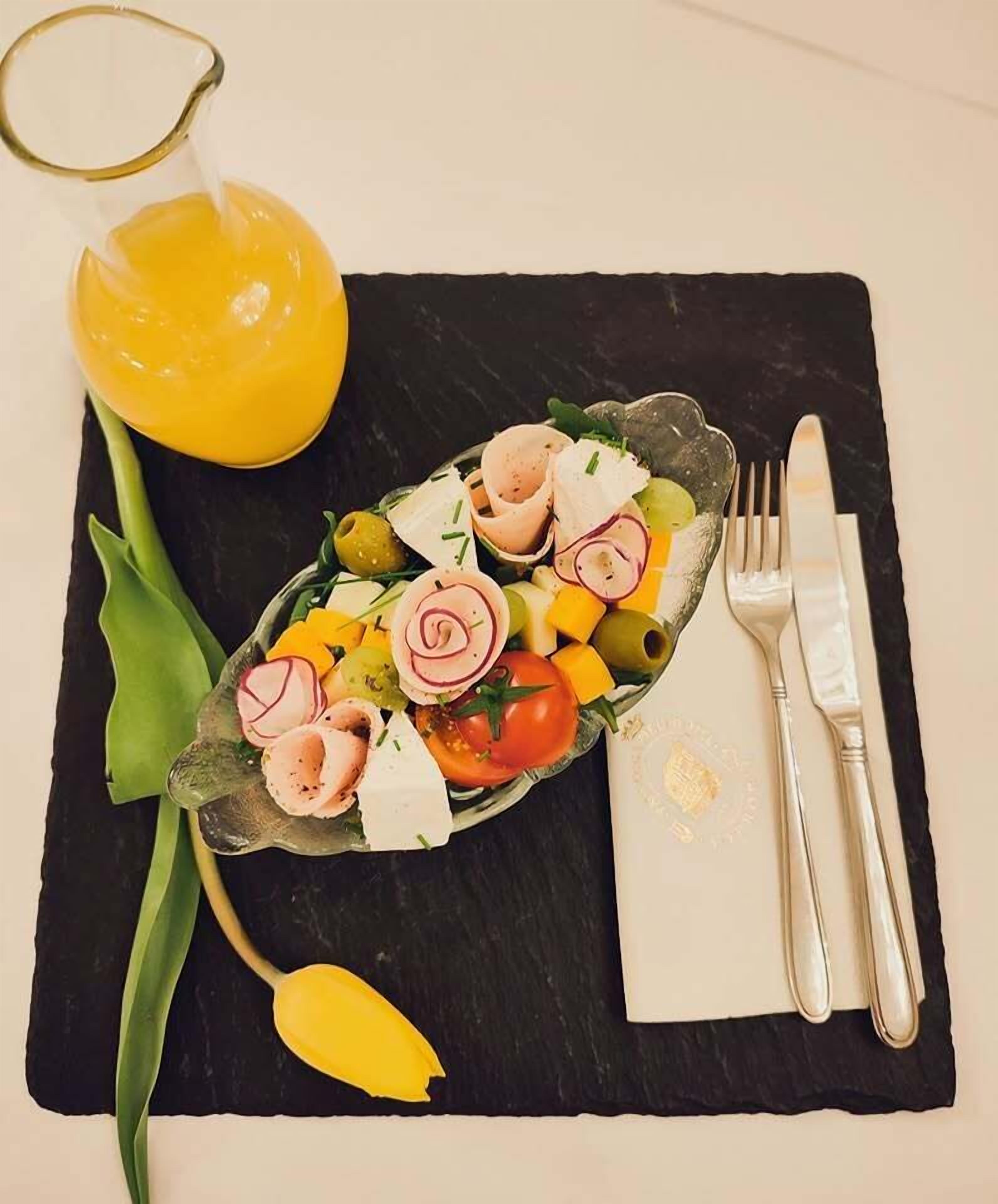 Una tabla de pizarra negra con una ensalada, una bebida amarilla y cubiertos sobre un paño blanco.