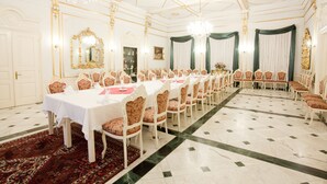 A formal dining room with a long table set for a banquet, surrounded by ornate chairs, chandeliers, and a patterned carpet. - Pannonia Hotel (Sopron)