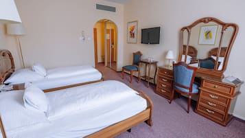 A hotel room with two single beds, a desk with a chair, a dresser, a television, and a mirror.