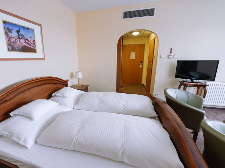 A neatly made bed with white linens, a television on a stand, and a framed picture on the wall.