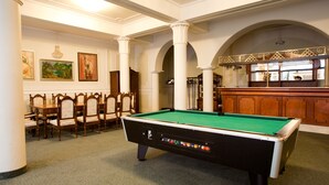 A pool table in a room with wooden chairs, a bar area, and framed artwork on the walls. - Pannonia Hotel (Sopron)