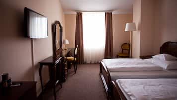 A hotel room with two beds, a desk with a chair, a television, a lamp, and a window with curtains.