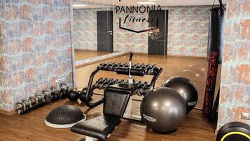 Une salle de sport avec un mur recouvert de miroirs, des kettlebells, des haltères et des ballons d’exercice.