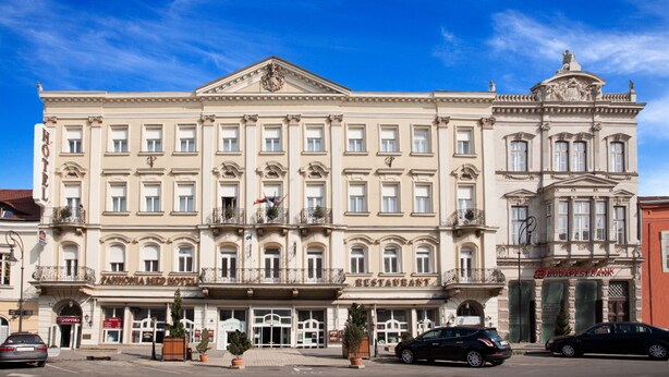 A large, historic building with multiple floors, featuring a prominent entrance with a canopy, a restaurant, and a bank. - Pannonia Hotel (Sopron)