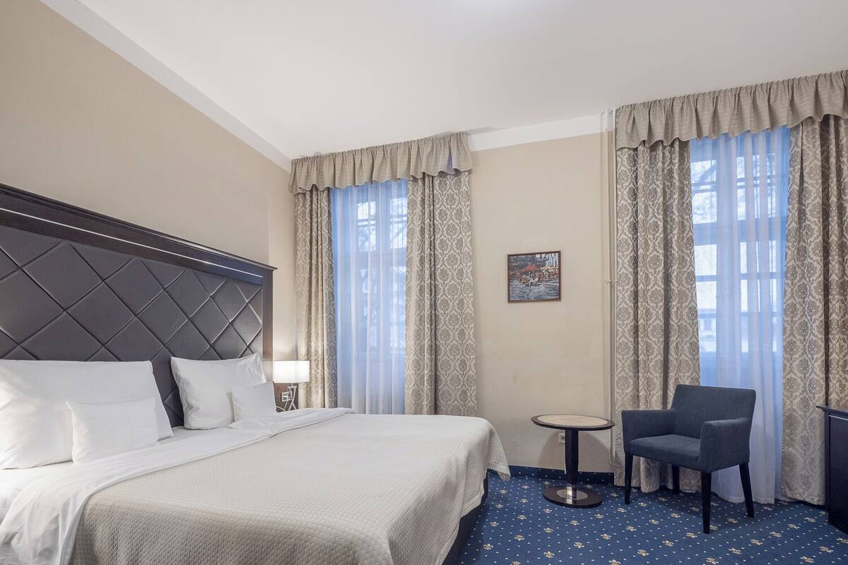 A hotel room with a large bed, a small round table, a chair, and a nightstand.