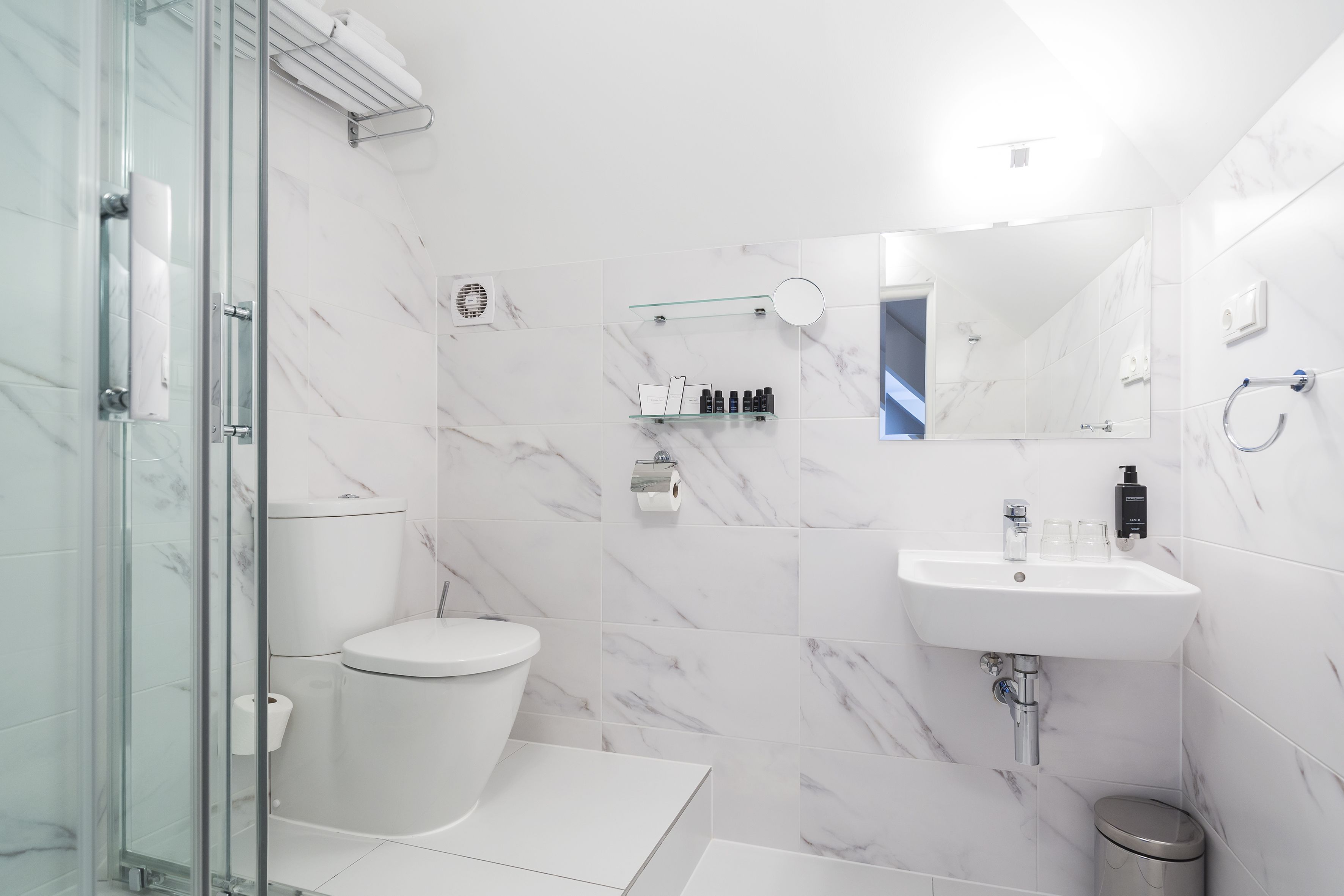 A modern bathroom with a glass shower enclosure, a white toilet, a sink with a mirror, and a toilet paper holder.