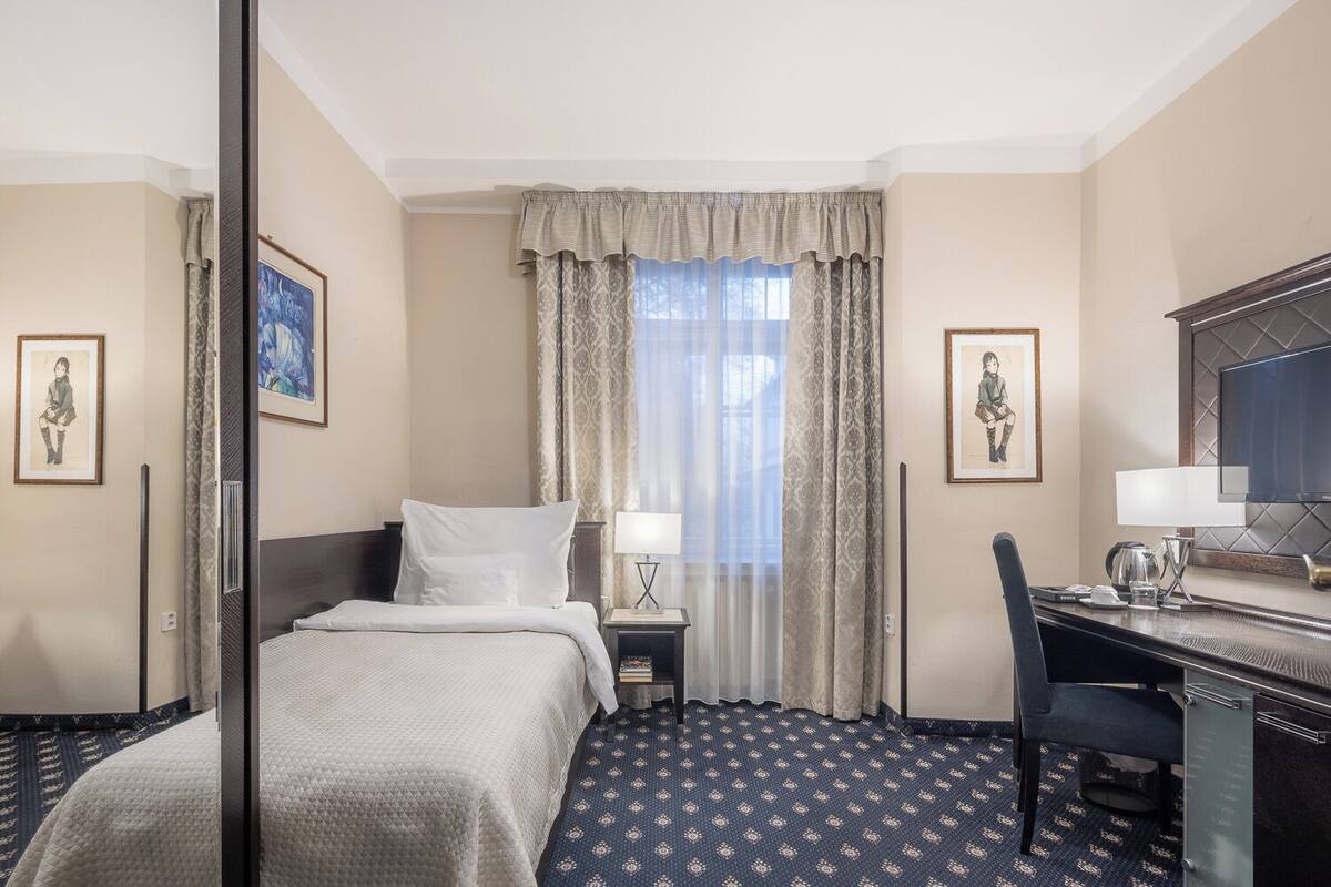 A hotel room with a bed, a desk with a chair, a TV, and artwork on the walls.