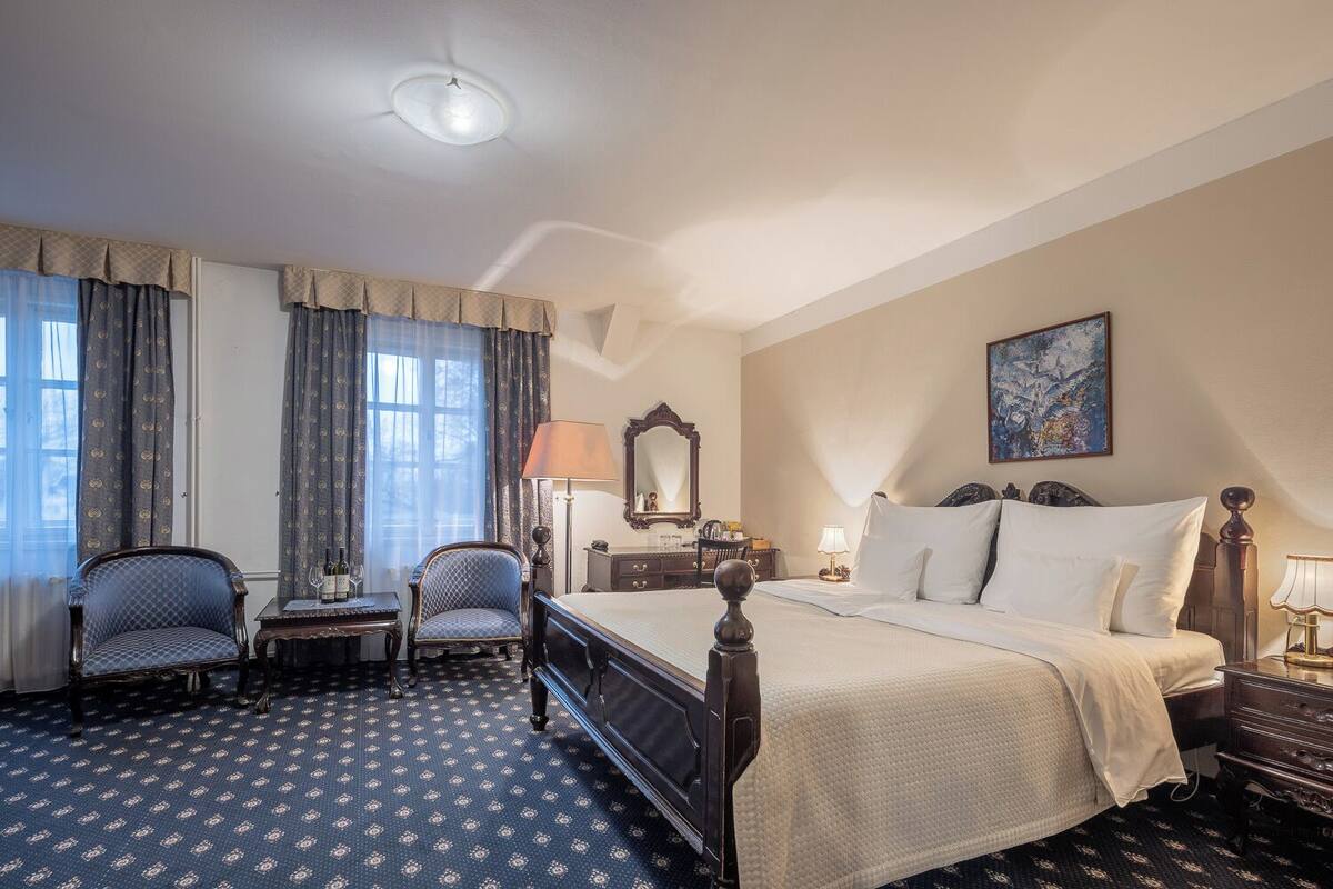 A hotel room with a bed, two armchairs, a dresser, a mirror, and a painting on the wall.
