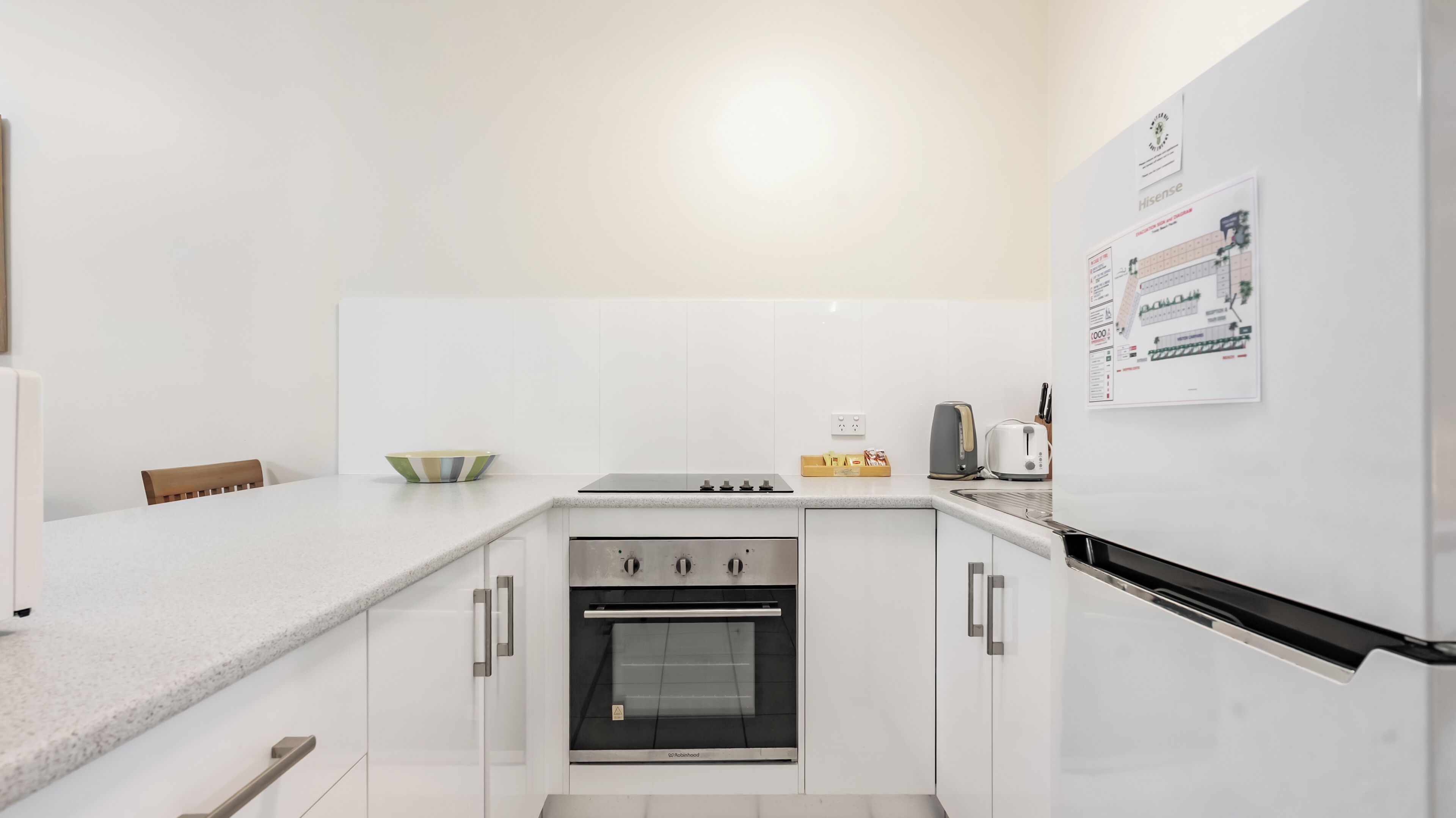 Una cocina moderna con armarios blancos, horno integrado, estufa y refrigerador.