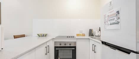 Una cocina moderna con armarios blancos, horno integrado, estufa y refrigerador.