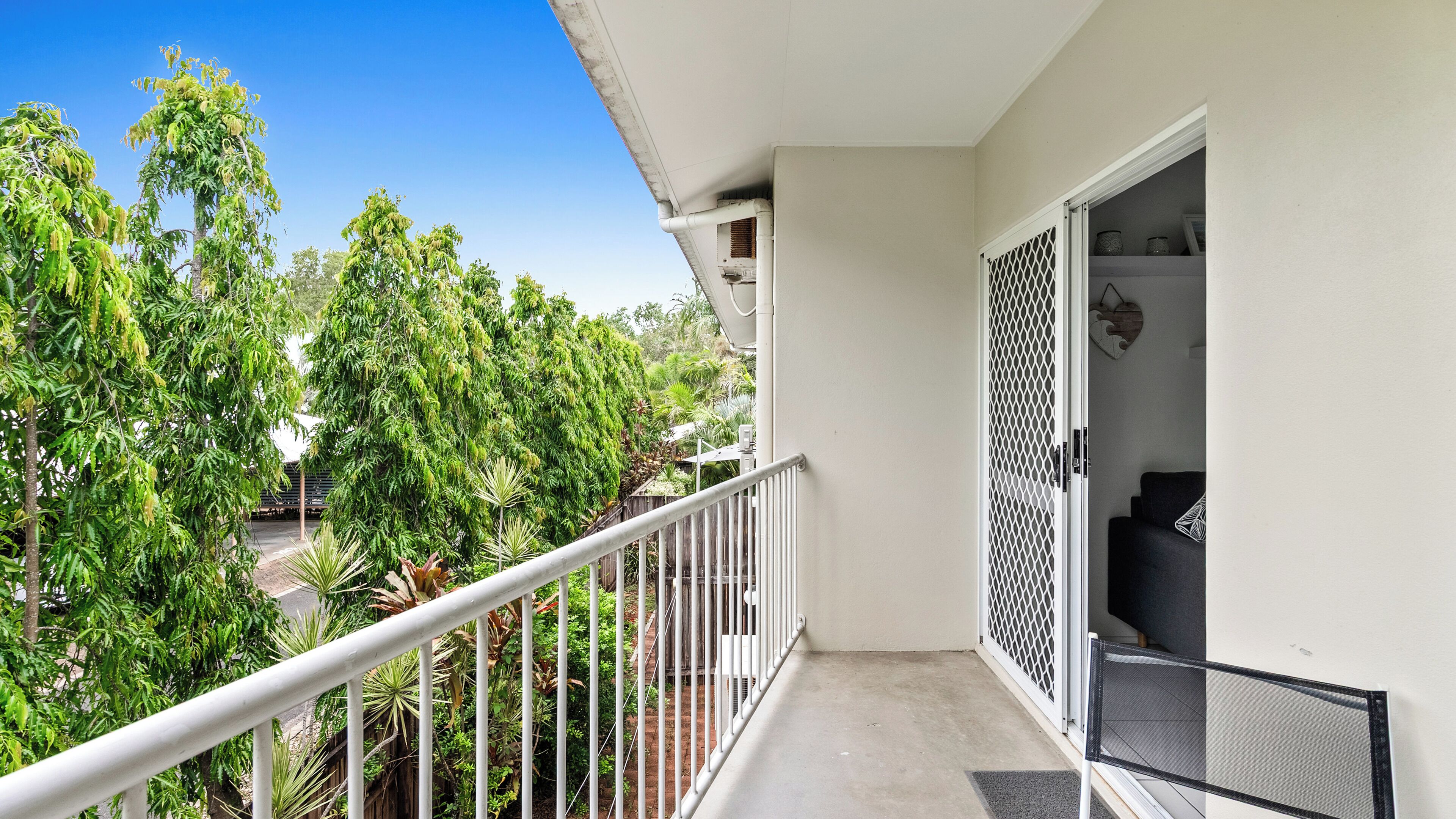 Ein Balkon mit weißer Brüstung, der auf einen Garten mit verschiedenen Bäumen und Pflanzen blickt.