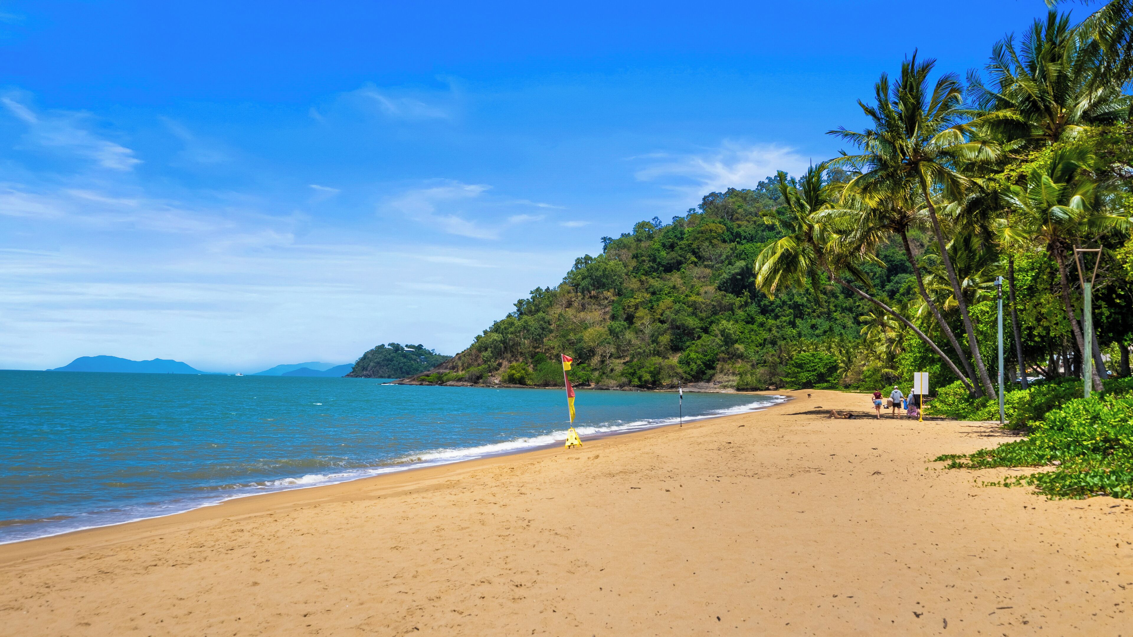 A beach with clear blue water, sandy shore, and lush greenery.
