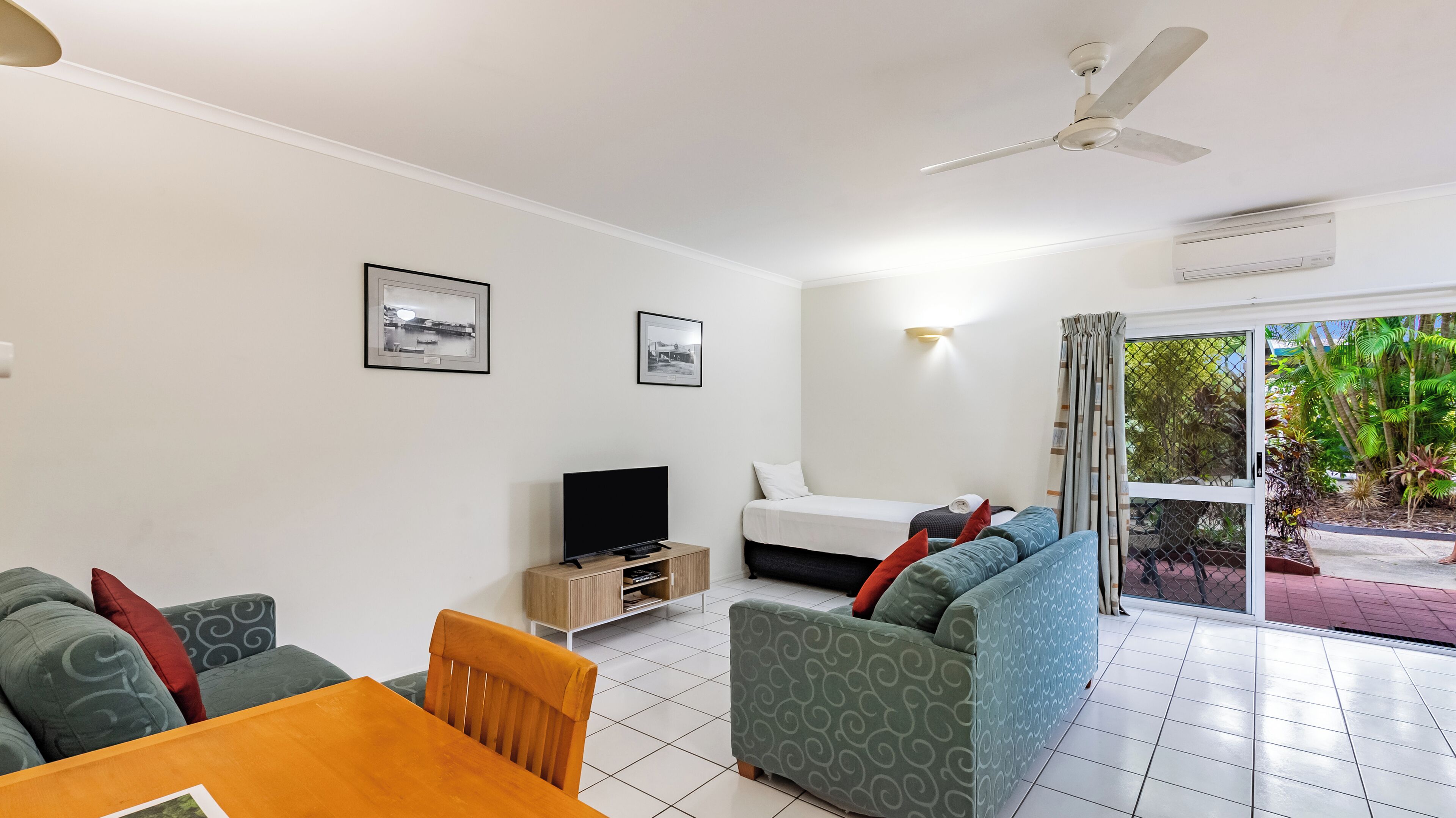 A modern hotel room with a flat-screen TV, a sofa, a dining table, and a ceiling fan.