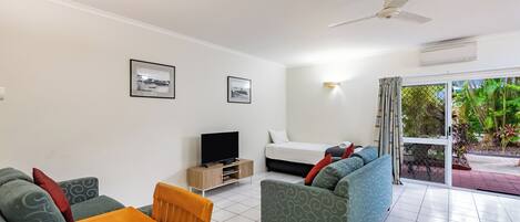 A modern hotel room with a flat-screen TV, a sofa, a dining table, and a ceiling fan.