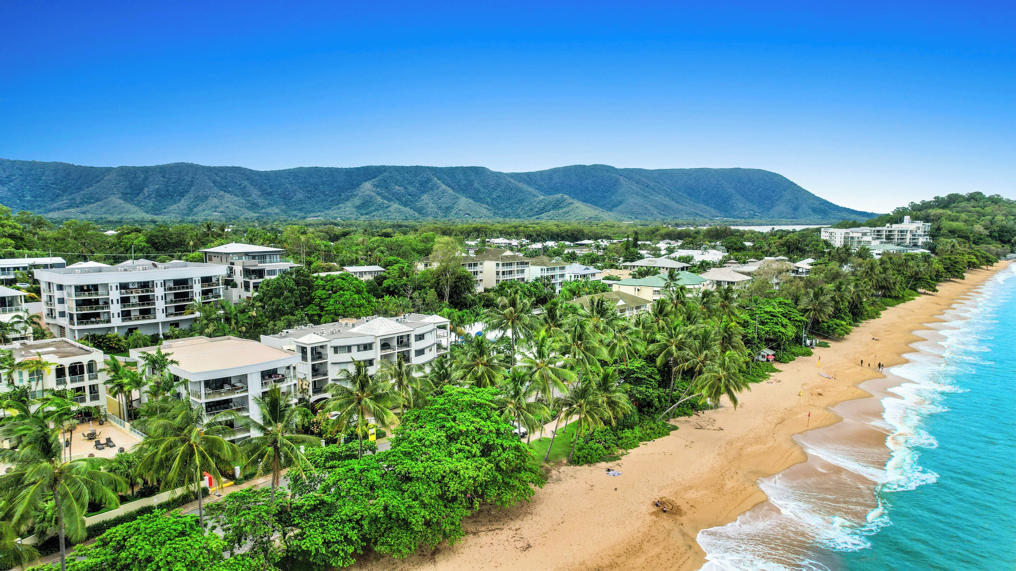 A coastal resort with beachfront villas, lush greenery, and a view of distant mountains.