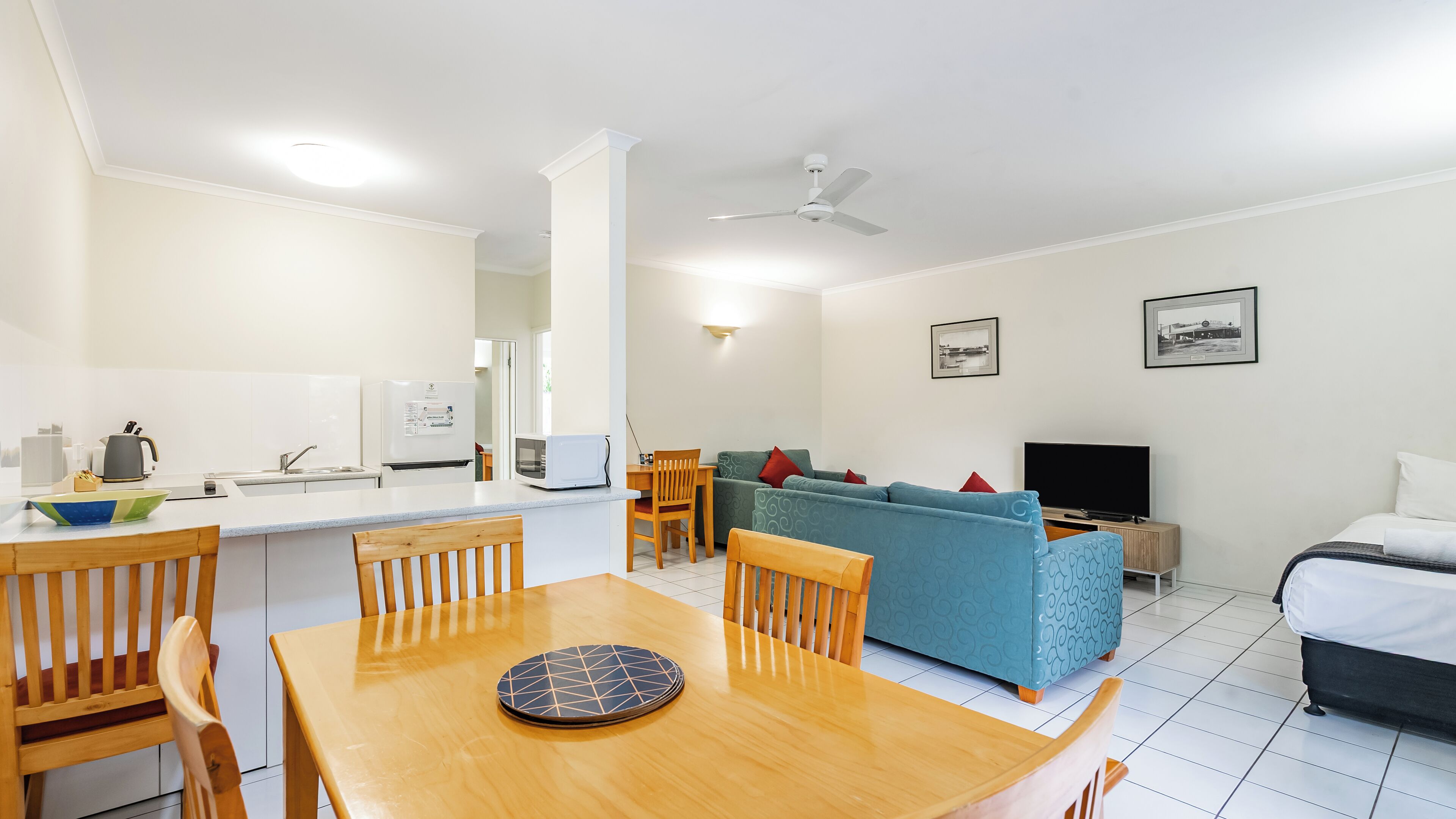 A compact living space with a dining area, kitchenette, sofa, TV, and a bed.