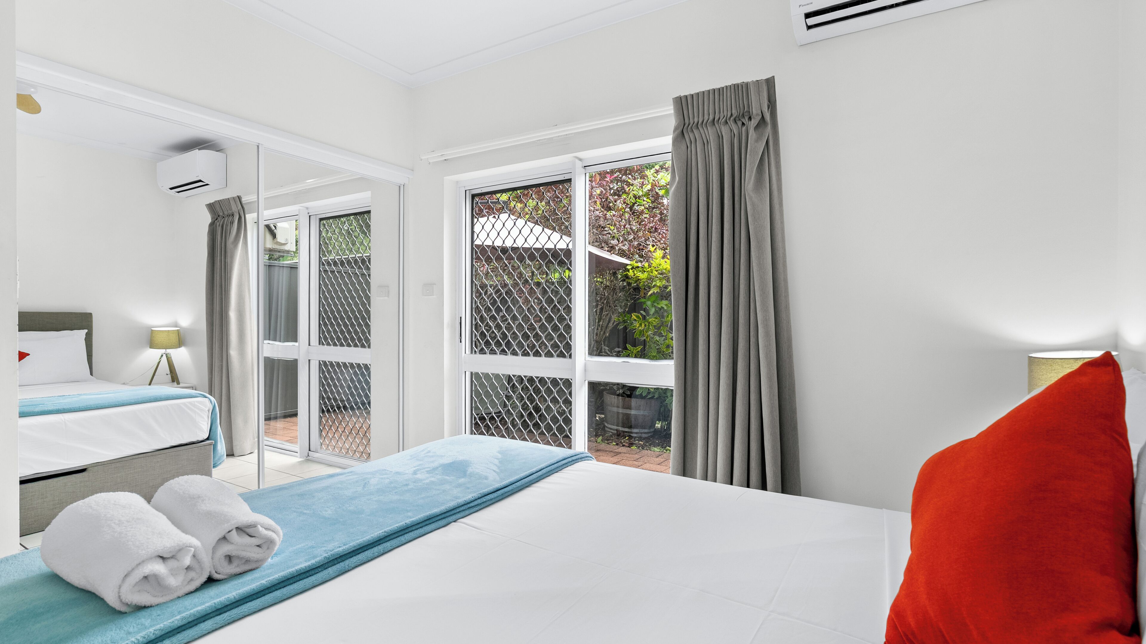 A hotel room with a bed, a window with a view of the outdoors, and a ceiling fan.