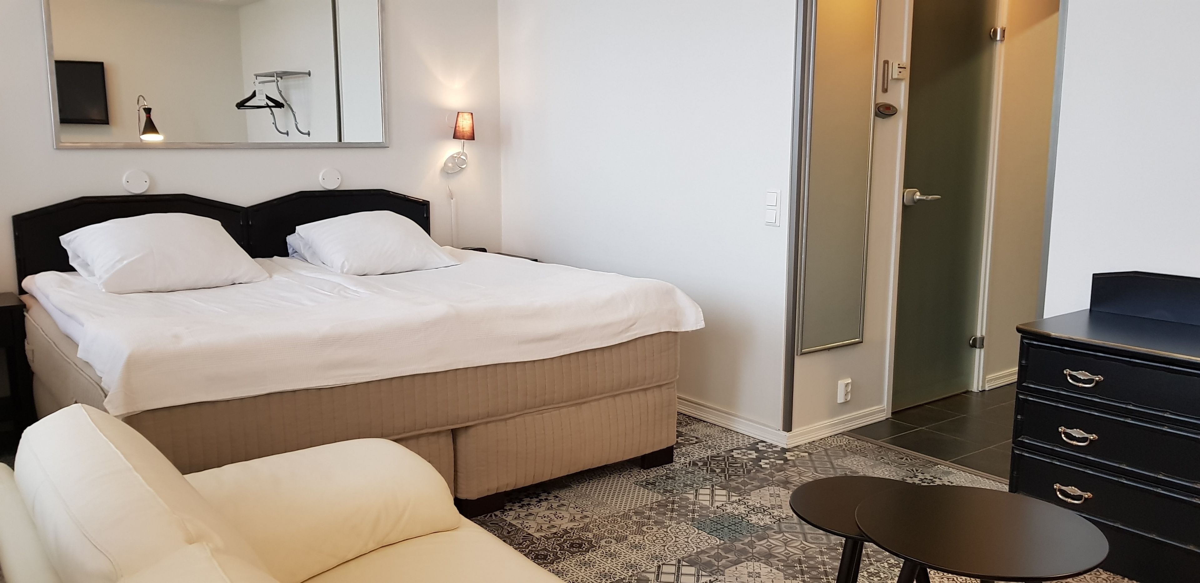A neatly arranged hotel room with a bed, bedside tables, a chair, a dresser, and a walk-in closet.