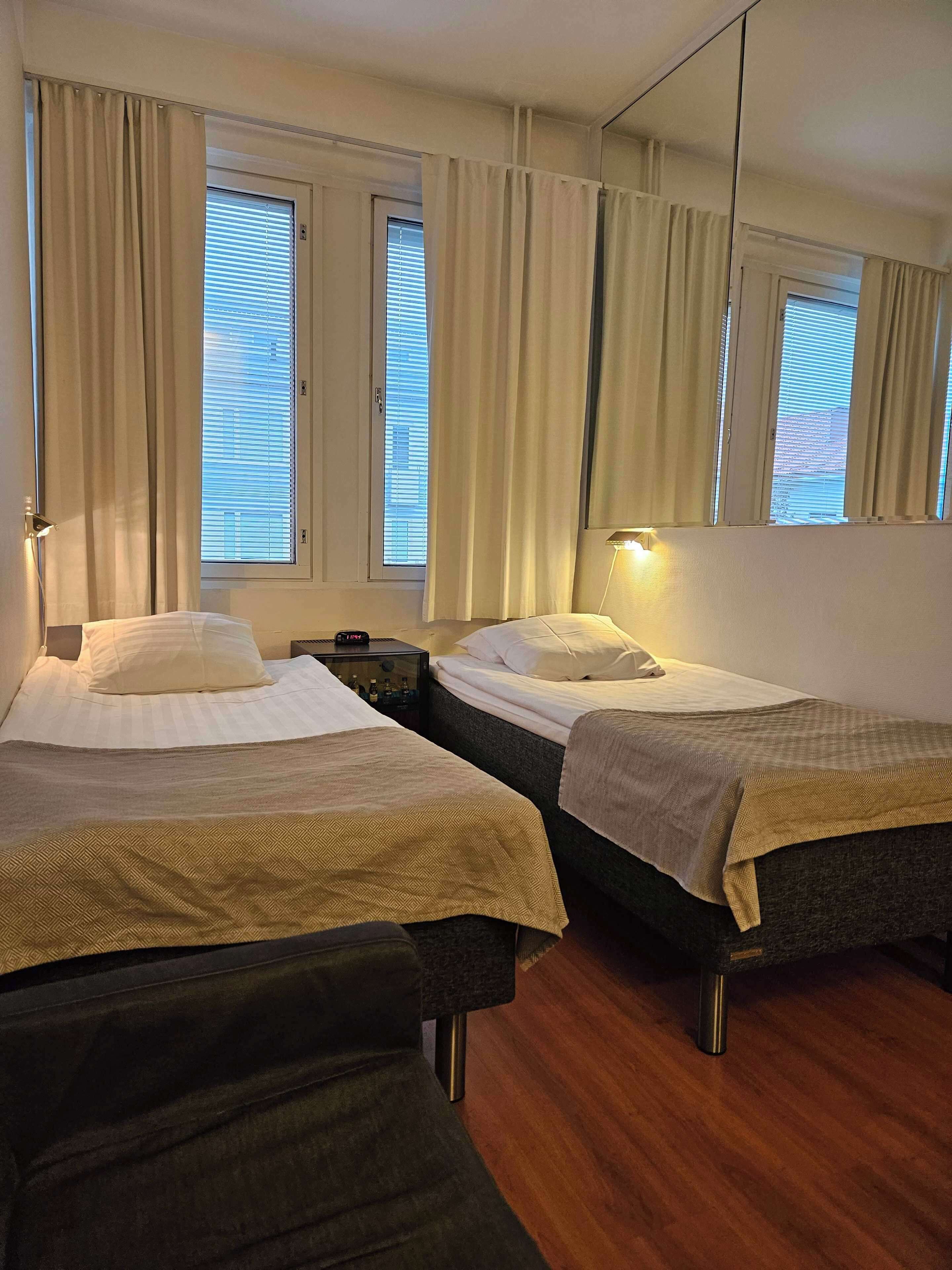 Ein Hotelzimmer mit zwei Betten, einem Nachttisch, einer Lampe und einem großen Spiegel.