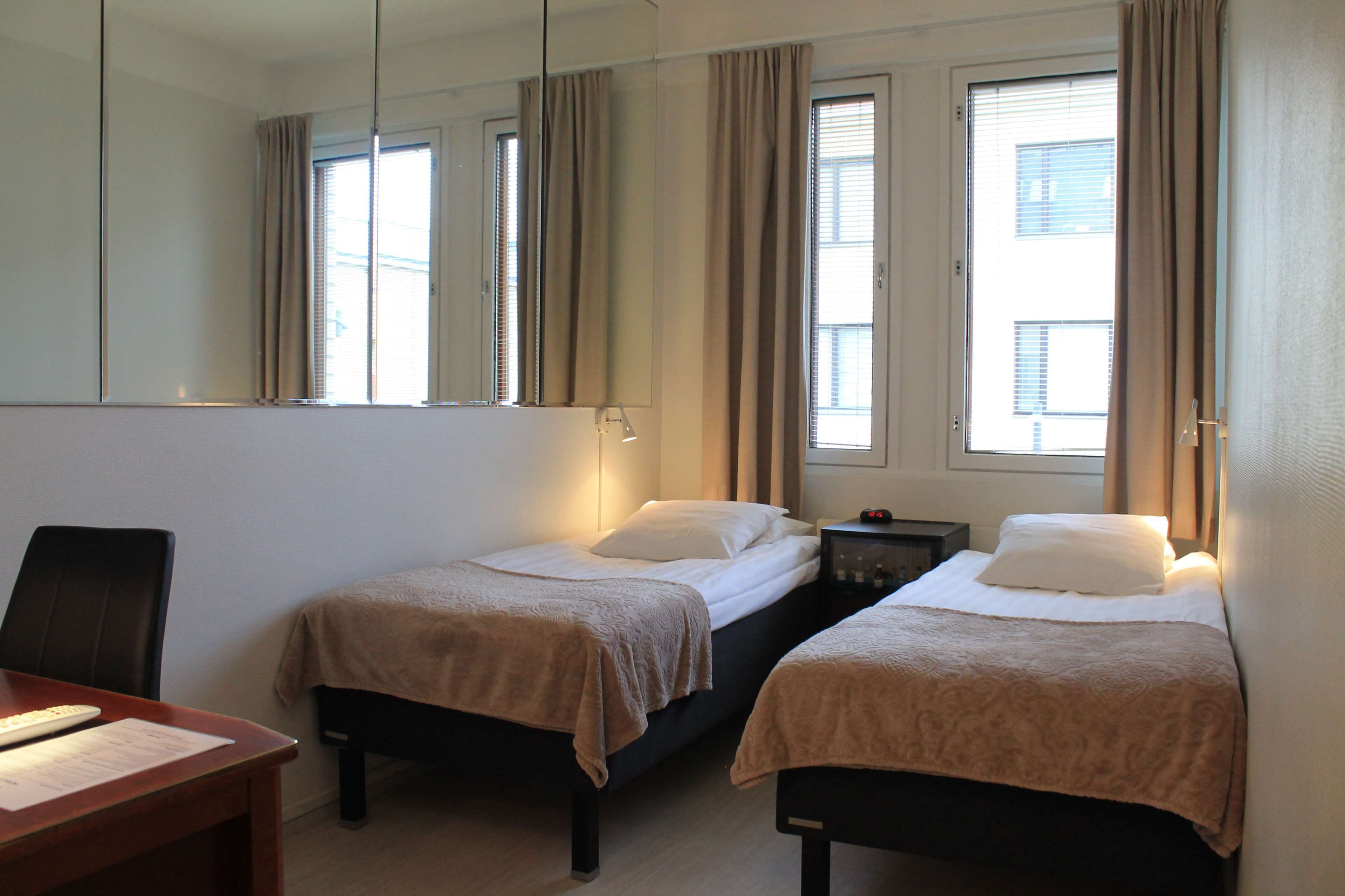 A hotel room with two beds, a desk, a chair, a nightstand, and a large mirror.