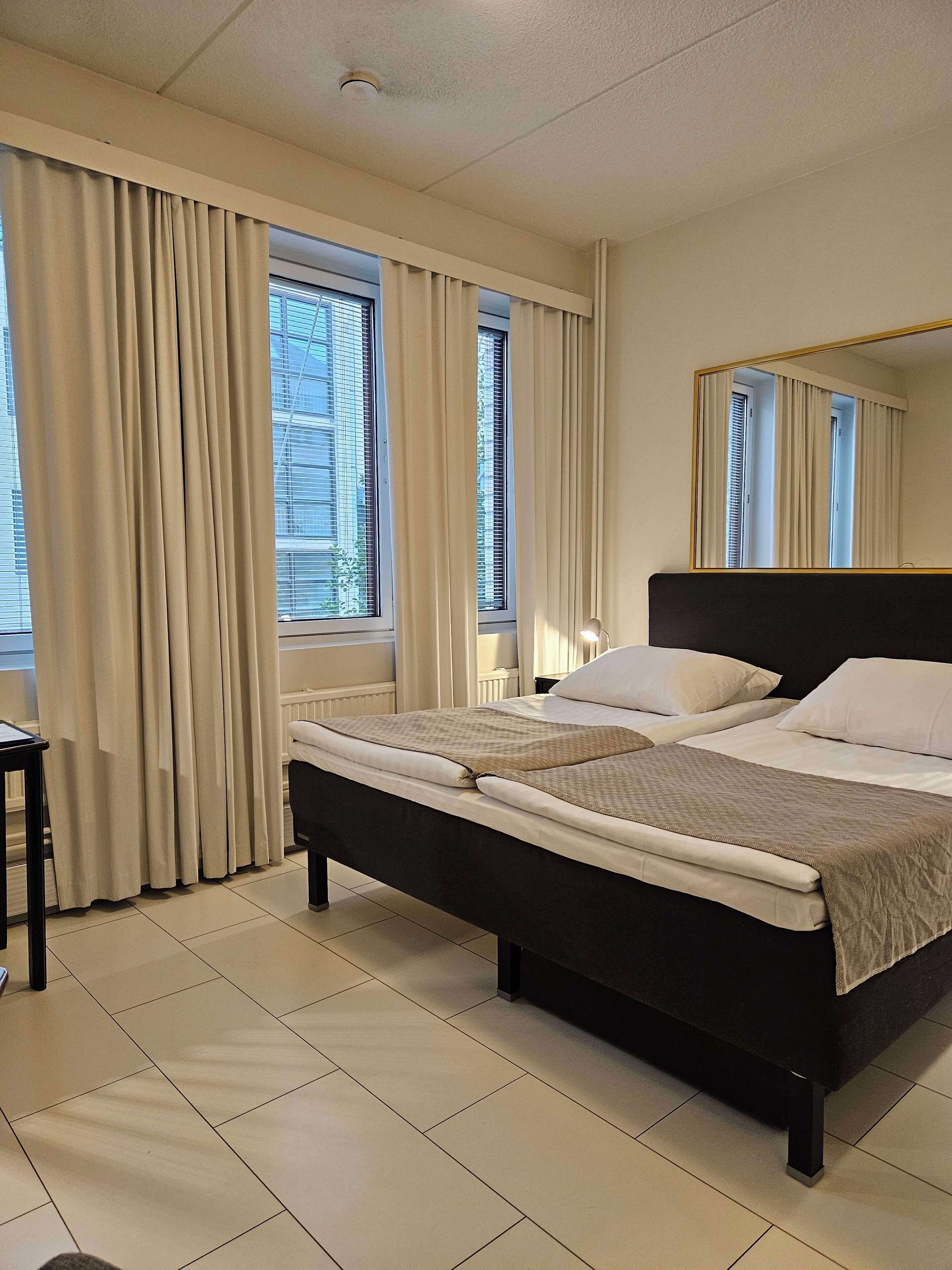 Una cama bien hecha con cabecera, mesita de noche y ventana con cortinas.