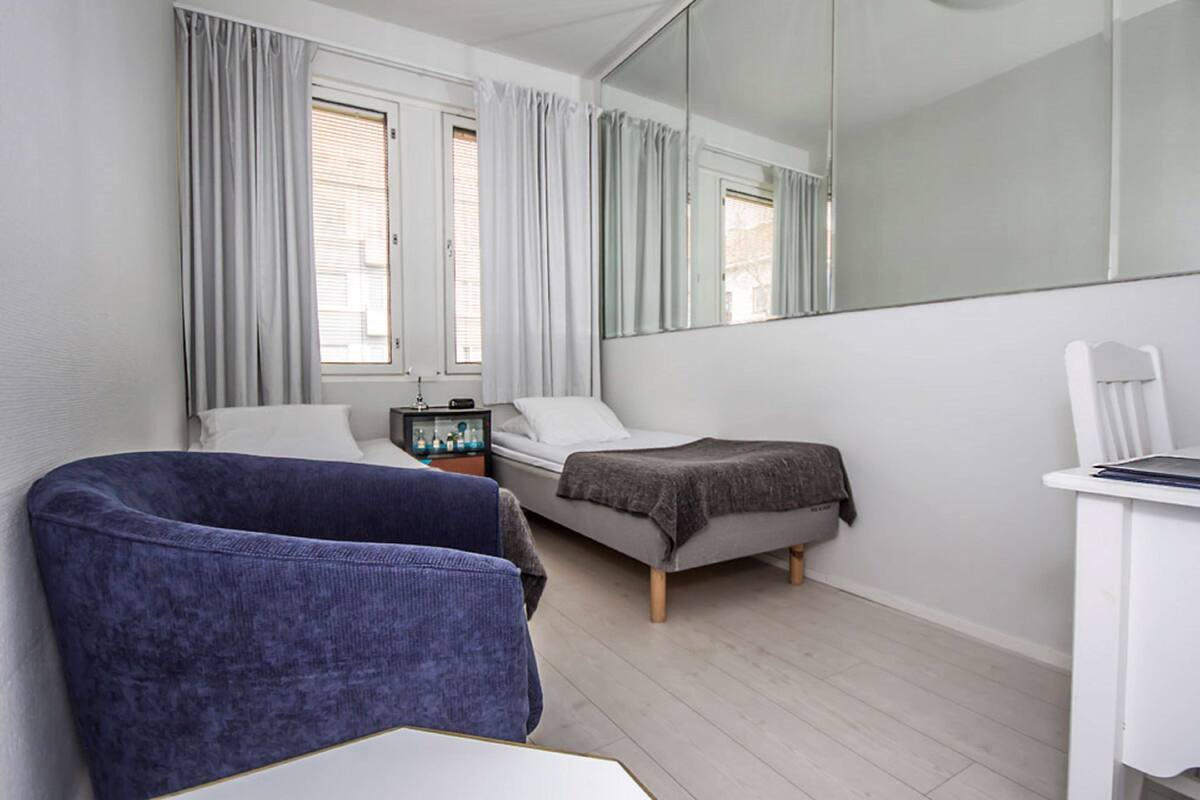 A hotel room with a bed, a chair, a desk, and a large mirror.