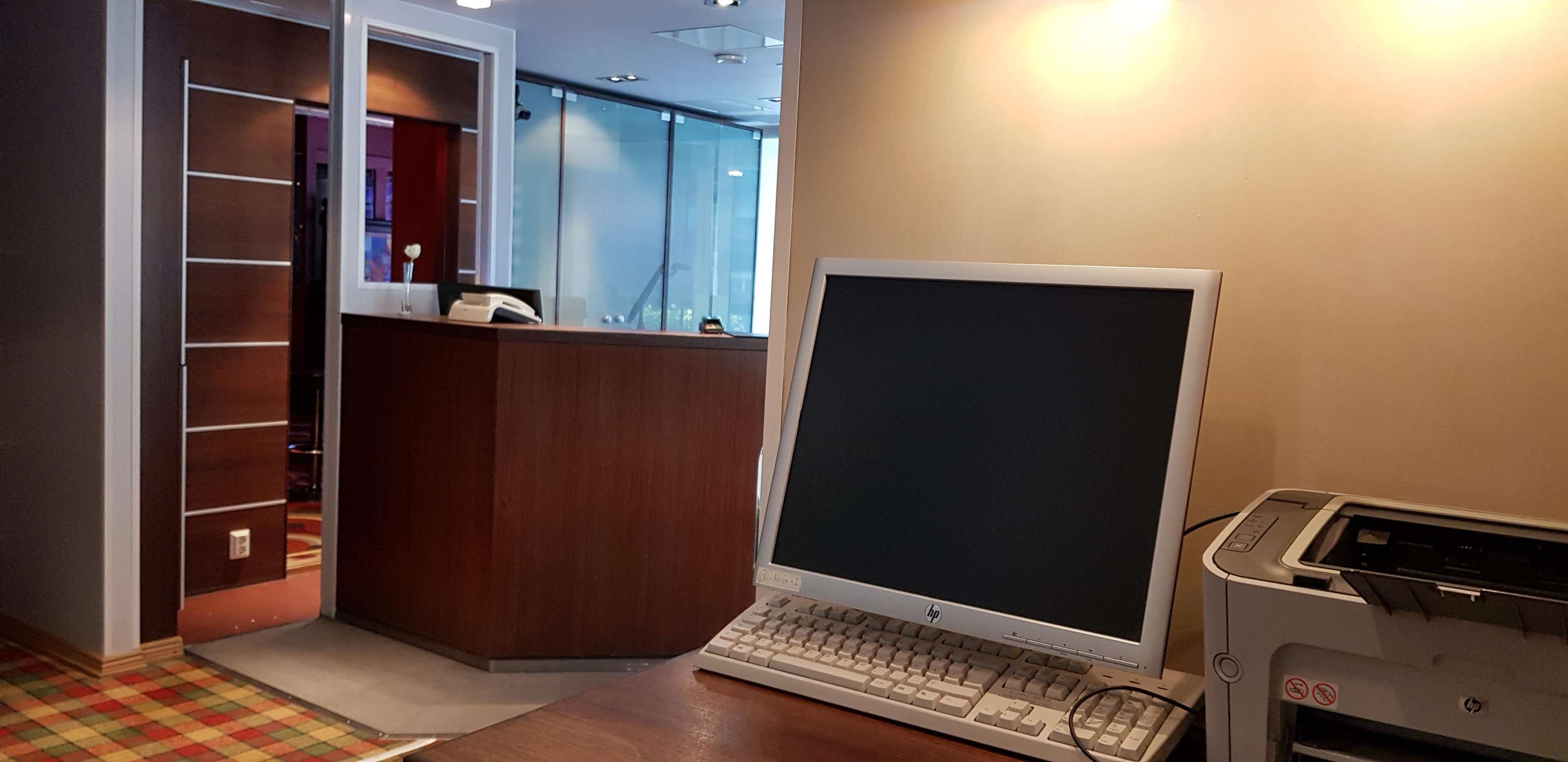 Zona de recepción de un hotel con un mostrador de madera, una computadora e impresora.