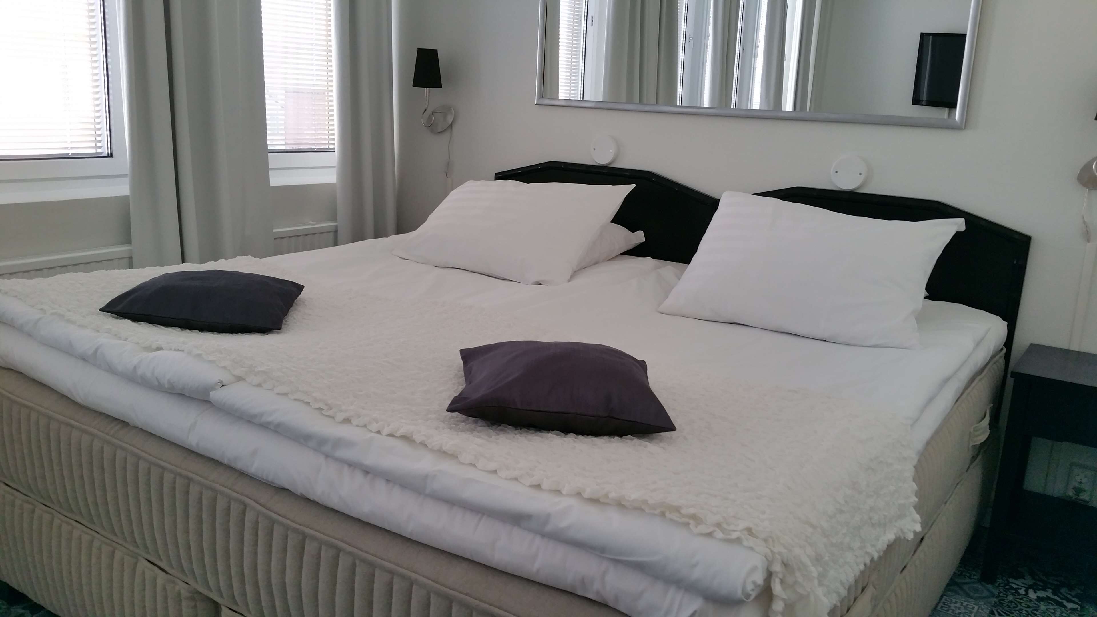 Una cama bien tendida con almohadas blancas y oscuras, un edredón blanco y una manta blanca con textura.