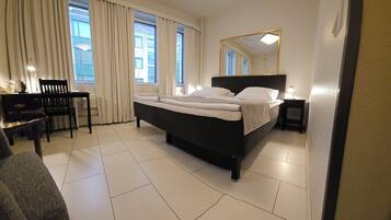 Een hotelkamer met een bed, een bureau, een stoel, een nachtkastje en een grote spiegel.