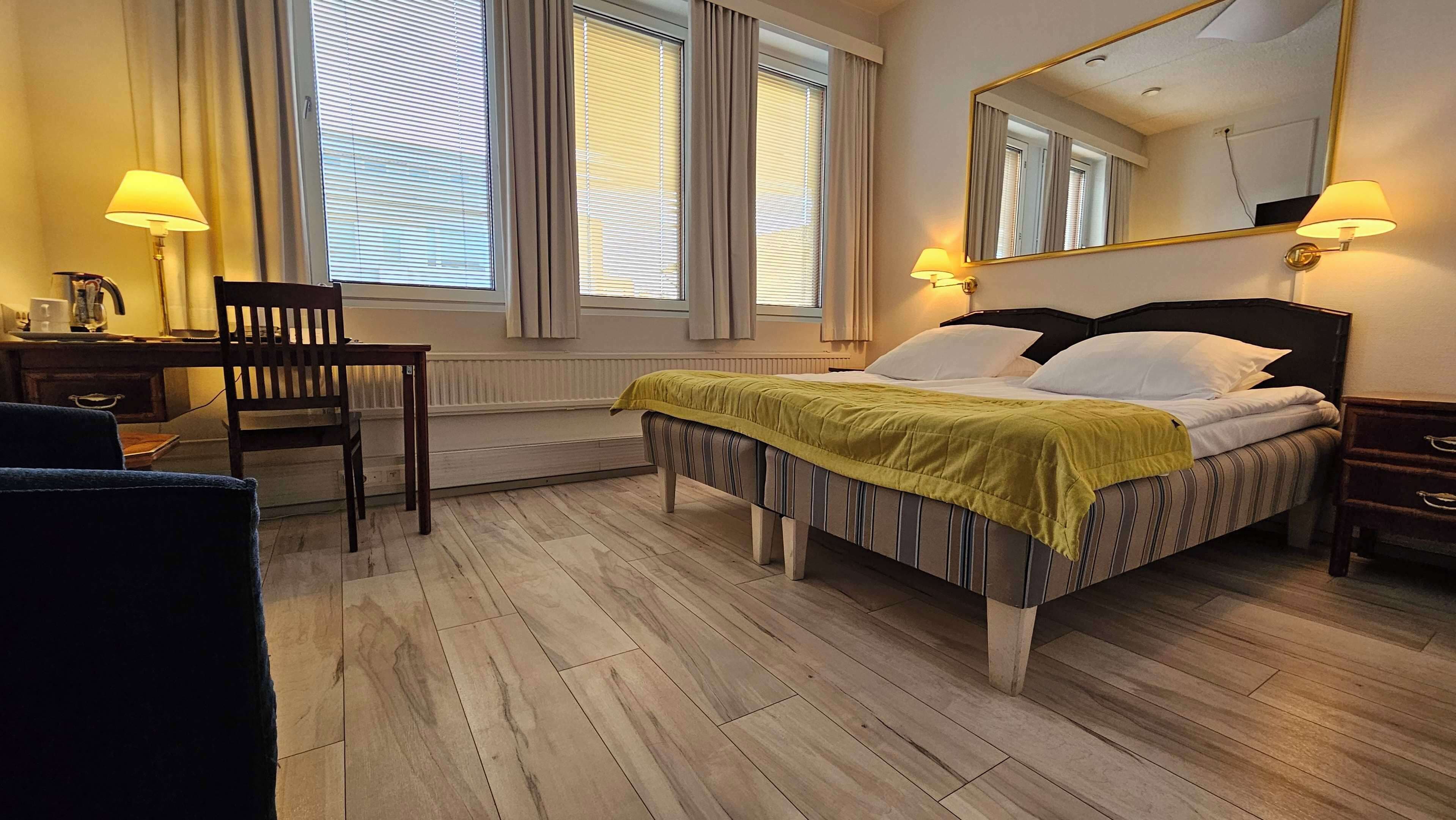 Ett hotellrum med en säng, en stol, ett skrivbord och en spegel.