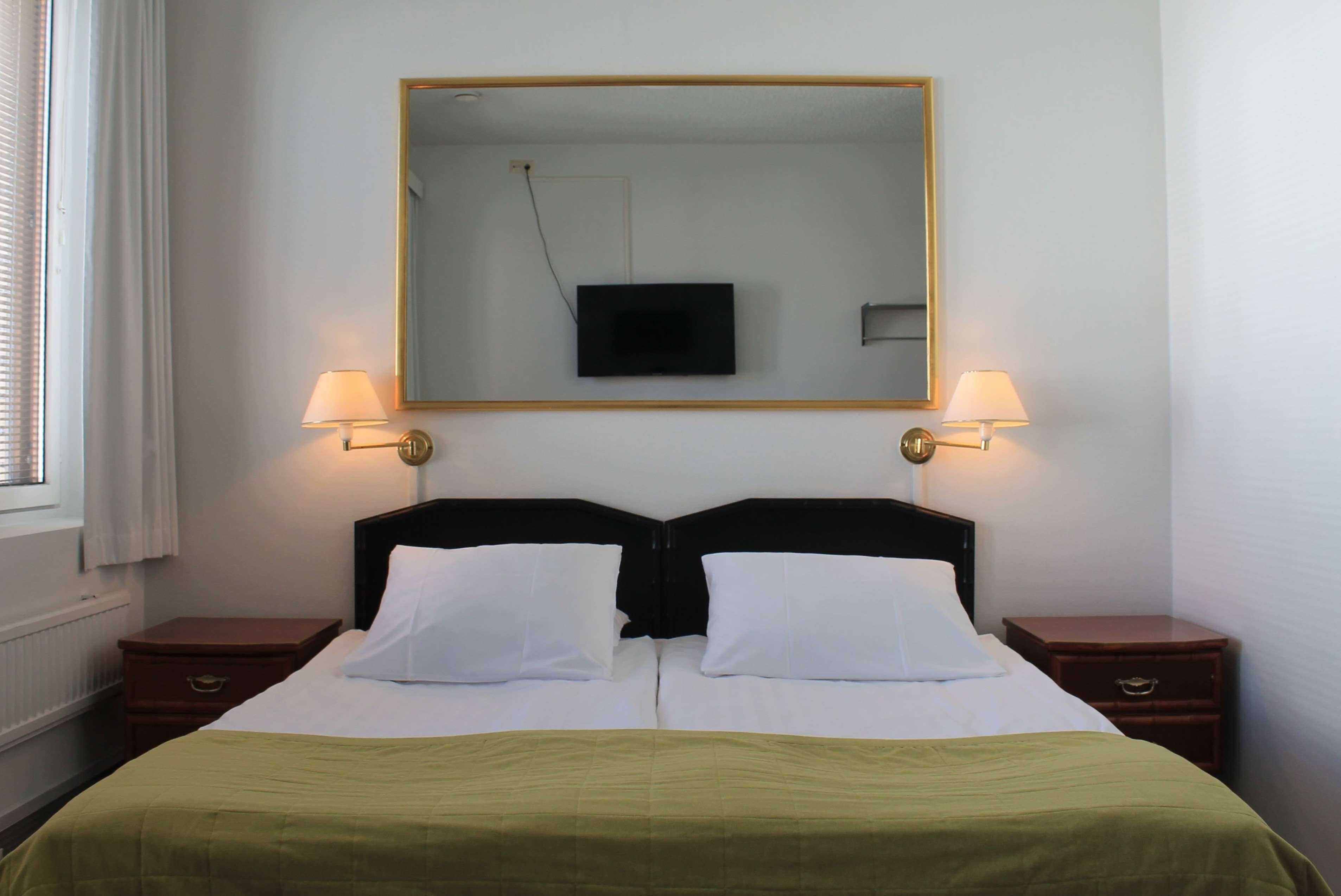 Una habitación de hotel con una cama, dos mesitas de noche, un televisor y un espejo en la pared.