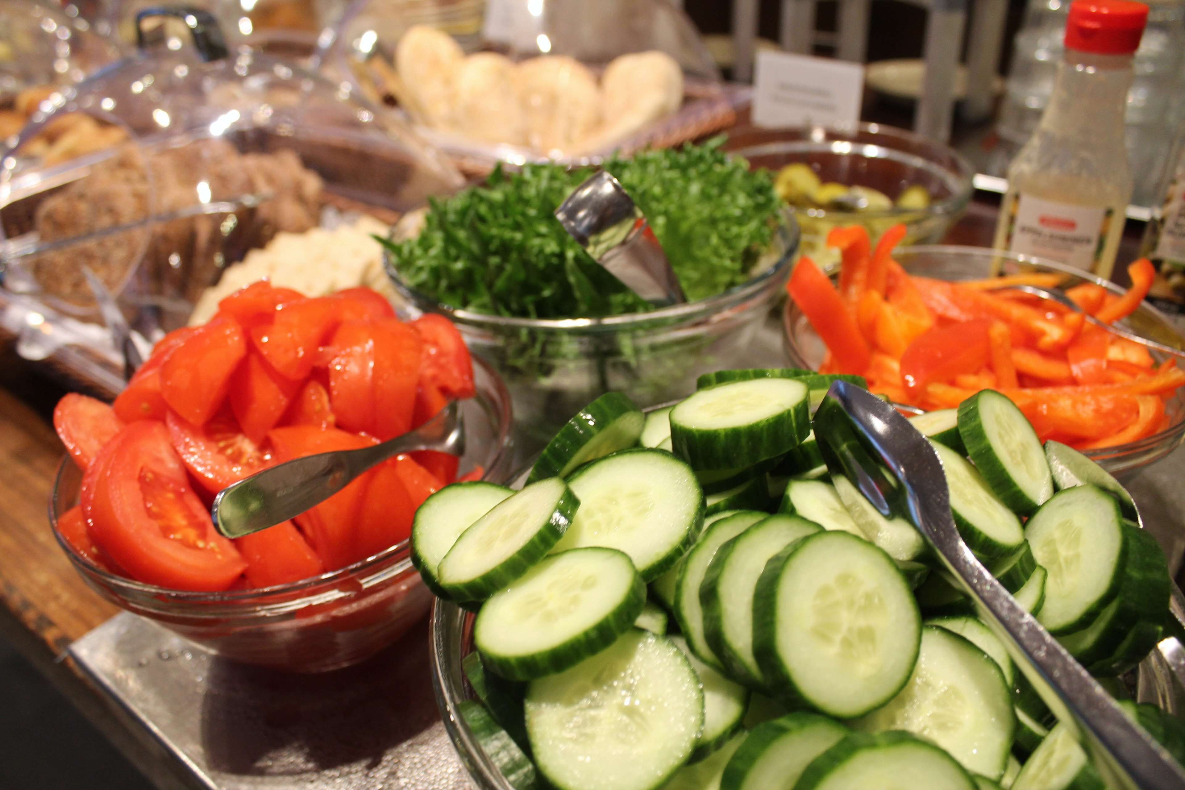 A buffet with various food items including sliced tomatoes, cucumbers, and leafy greens.