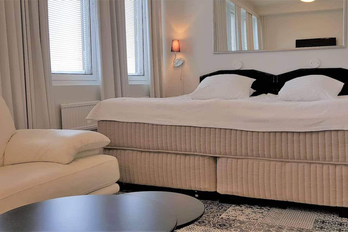 A neatly arranged bedroom with a large bed, a sofa, a bedside table, and a nightstand.
