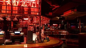 Un espace bar doté d’un comptoir incurvé, de tabourets de bar et de diverses bouteilles et verres disposés sur des étagères.