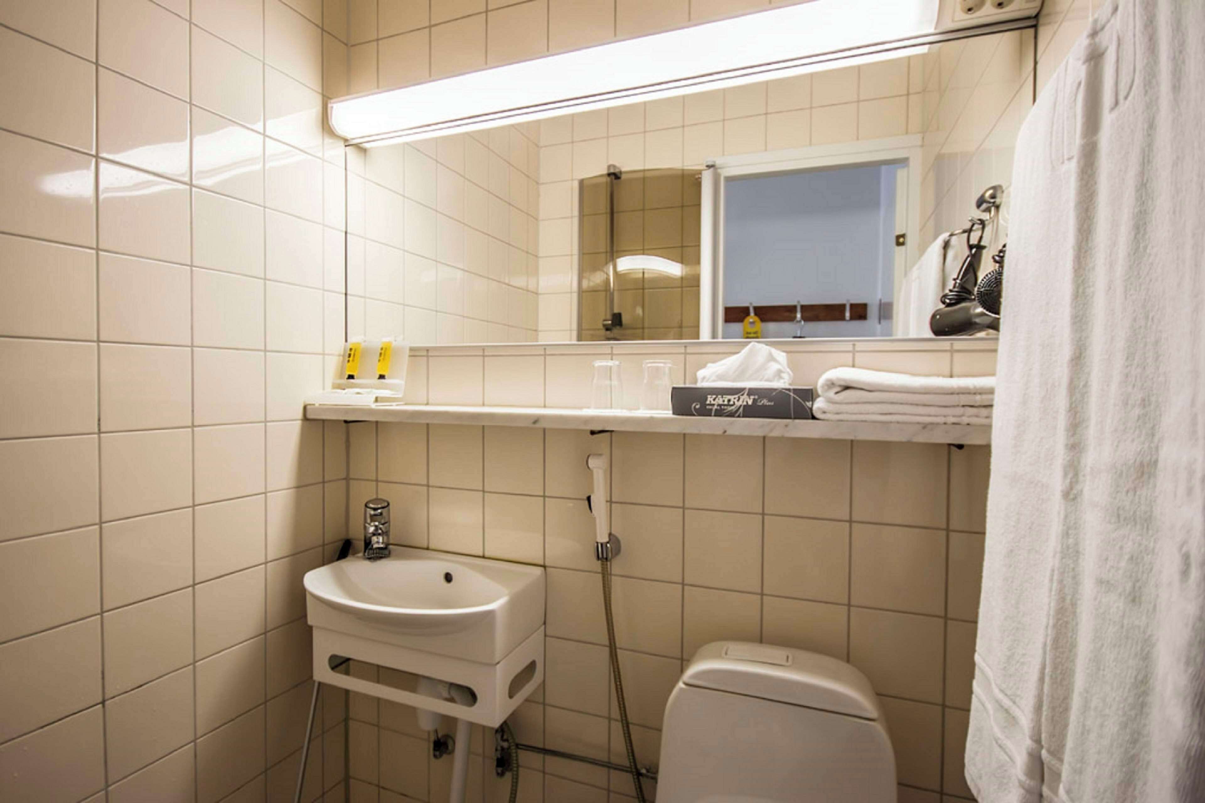 A bathroom with a white sink, toilet, and mirror. There is a towel rack with towels and a shelf with toiletries.