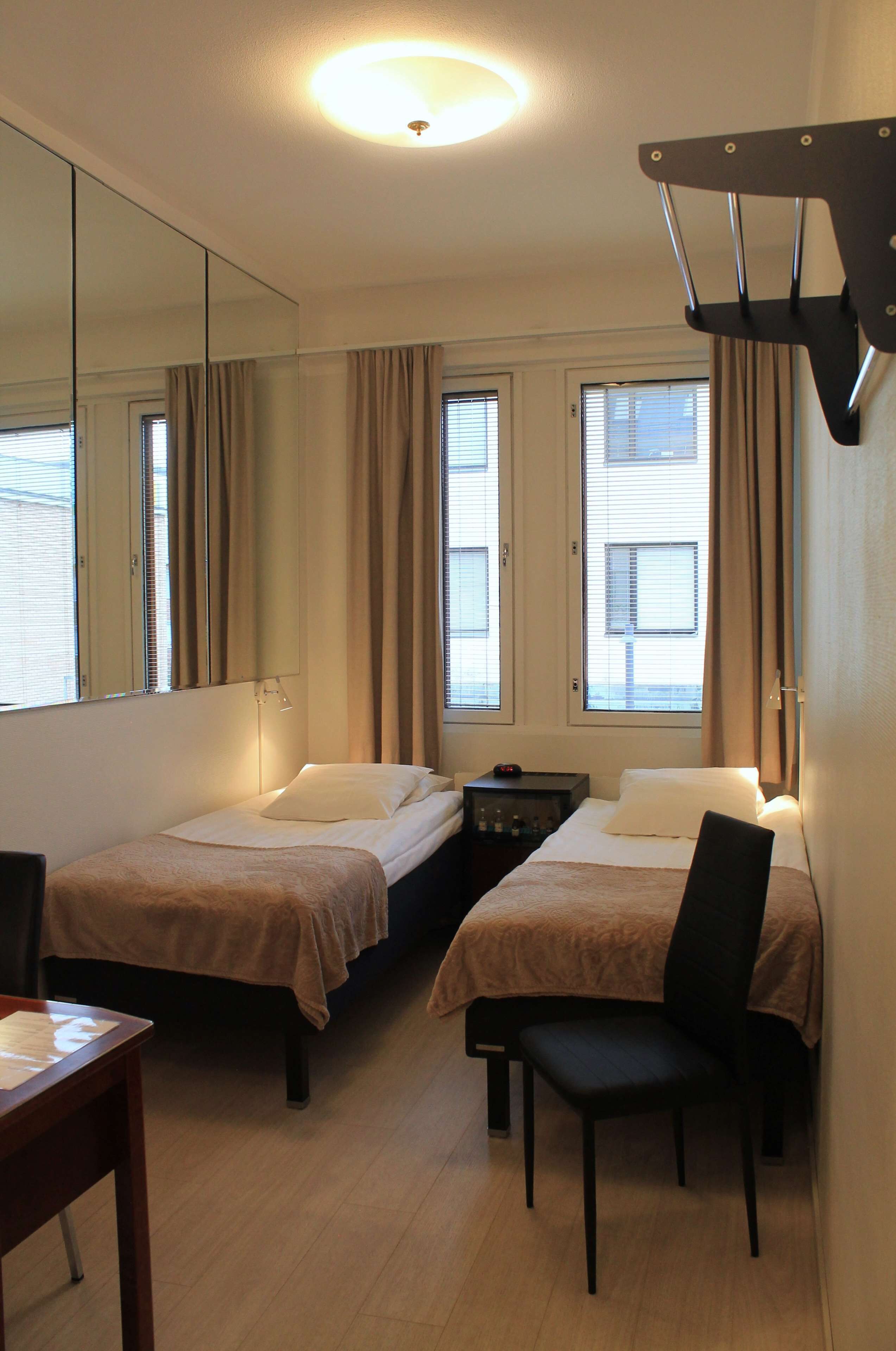 A hotel room with two single beds, a desk, a chair, and a large mirror.