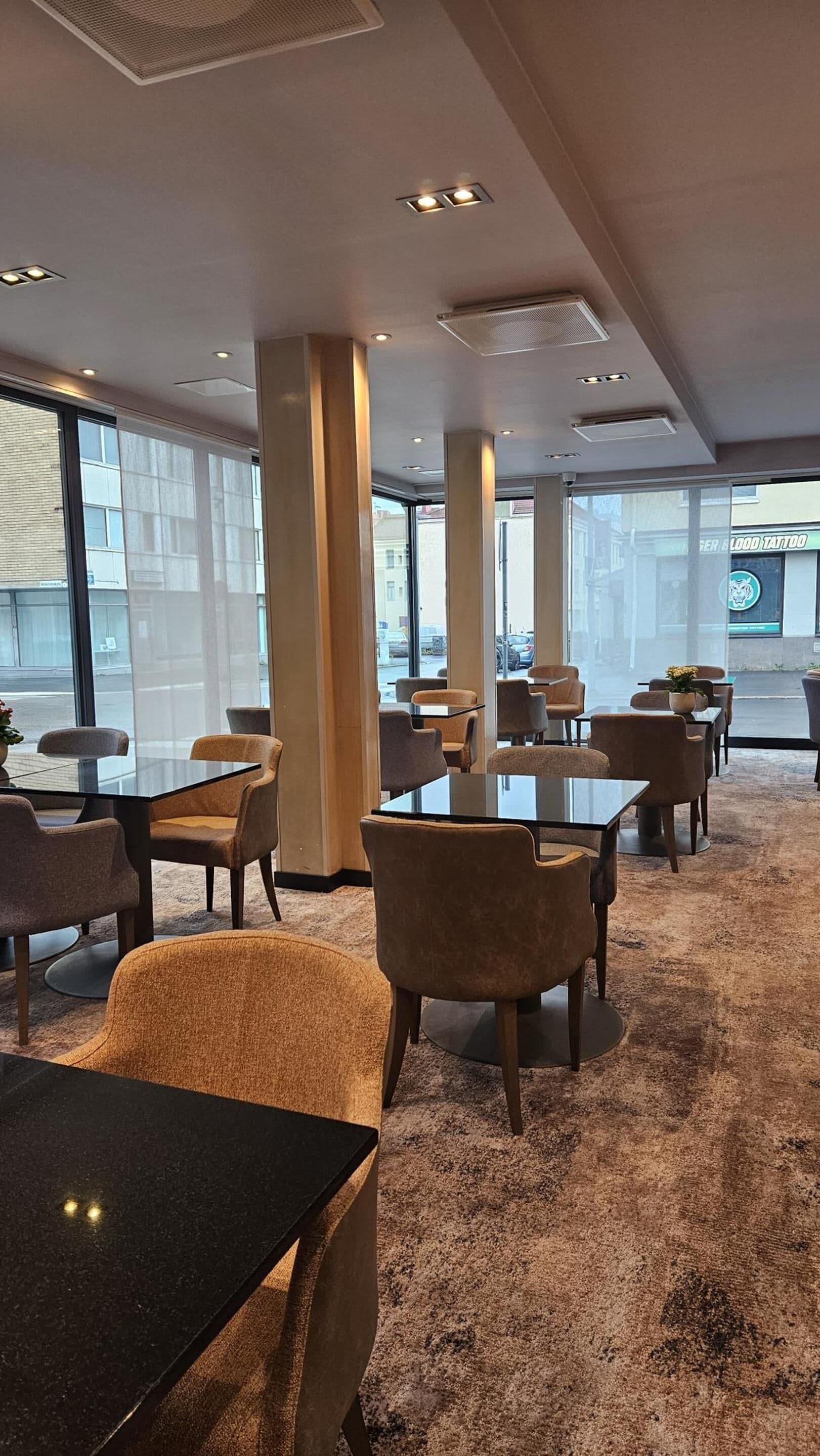 Un espace de détente intérieur moderne, doté de tables et de chaises, de grandes fenêtres et offrant une vue sur la rue.